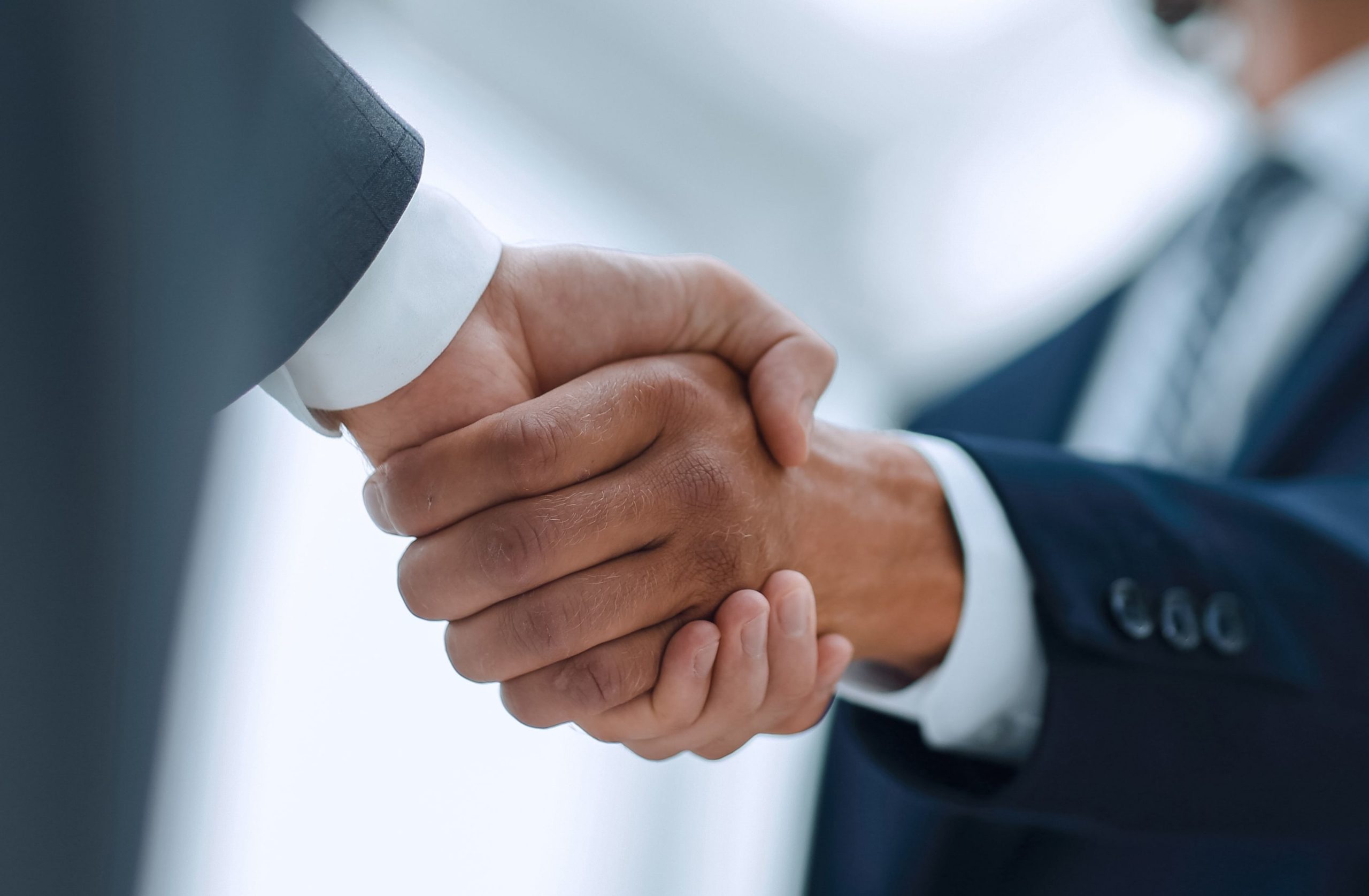 Zbliżenie na uścisk dłoni dwóch mężczyzn w garniturach, reprezentujący zaufanie i profesjonalne partnerstwo w biznesie.